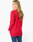 A woman wearing a bright red waffle-knit long-sleeve top and blue jeans, shown from a side-back angle against a plain white studio background.