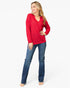 A woman modeling a bright red long-sleeve ribbed knit top with blue jeans against a plain white studio background.