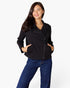 A woman modeling a black asymmetrical zipper jacket with side pockets, paired with blue jeans, against a plain white studio background.