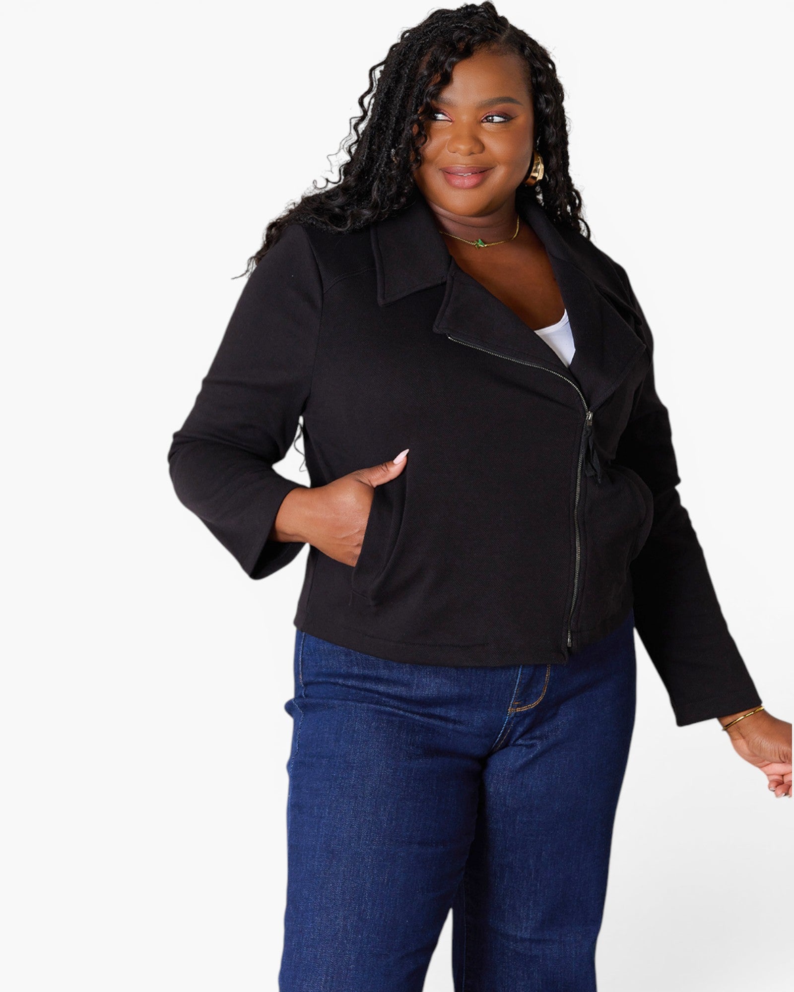 A woman modeling a black zip-front jacket with side pockets, paired with blue jeans, against a plain white studio background.