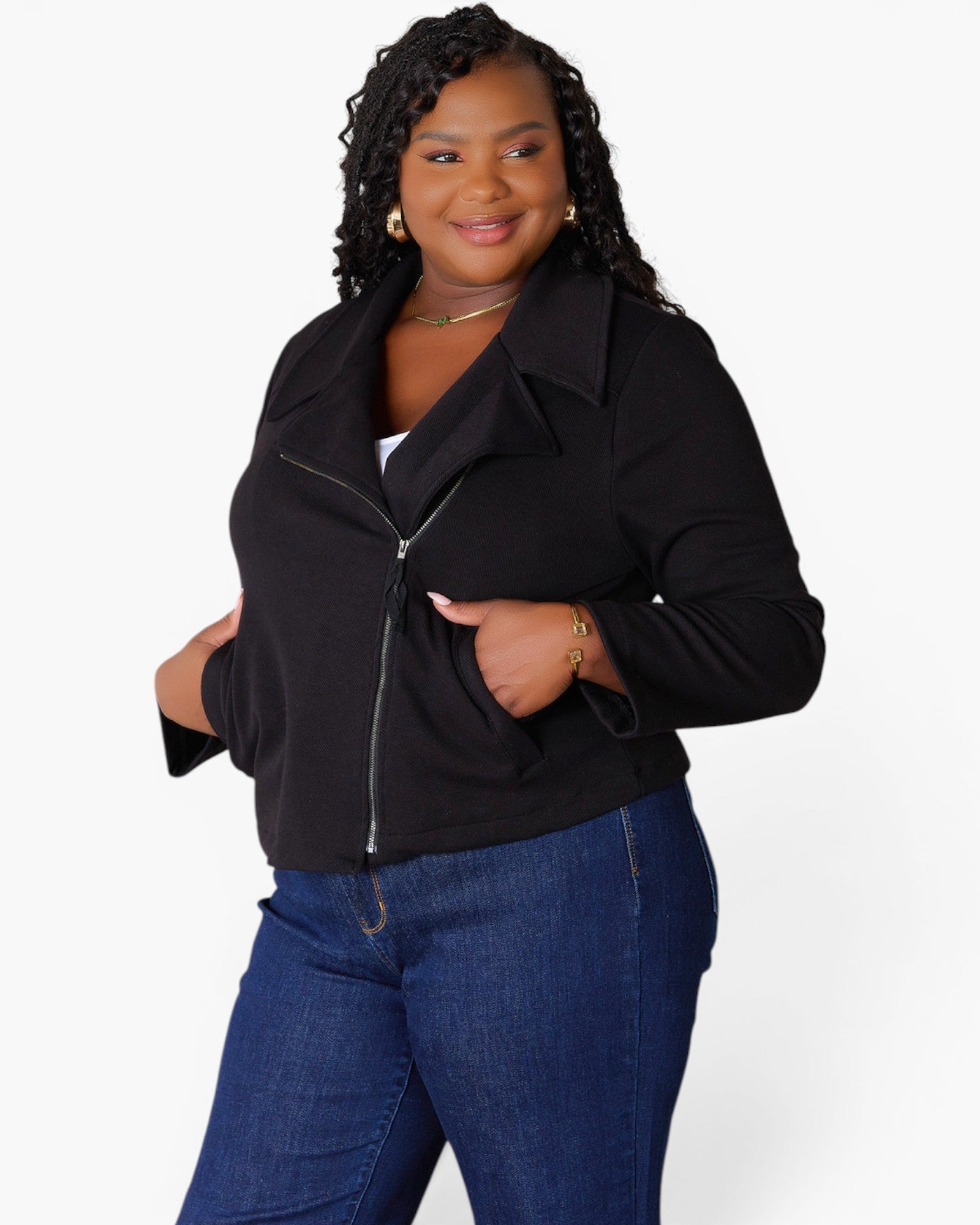 A woman modeling a black zip-up jacket with a wide collar and front pockets, paired with blue jeans, against a plain light gray studio background.