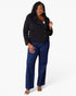 A woman modeling a black zip-front jacket and dark blue wide-leg jeans against a plain light gray studio background.