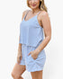 A woman wearing a sleeveless blue and white striped romper with thin shoulder straps, a V-neckline, and short legs with side pockets, photographed against a plain light background.