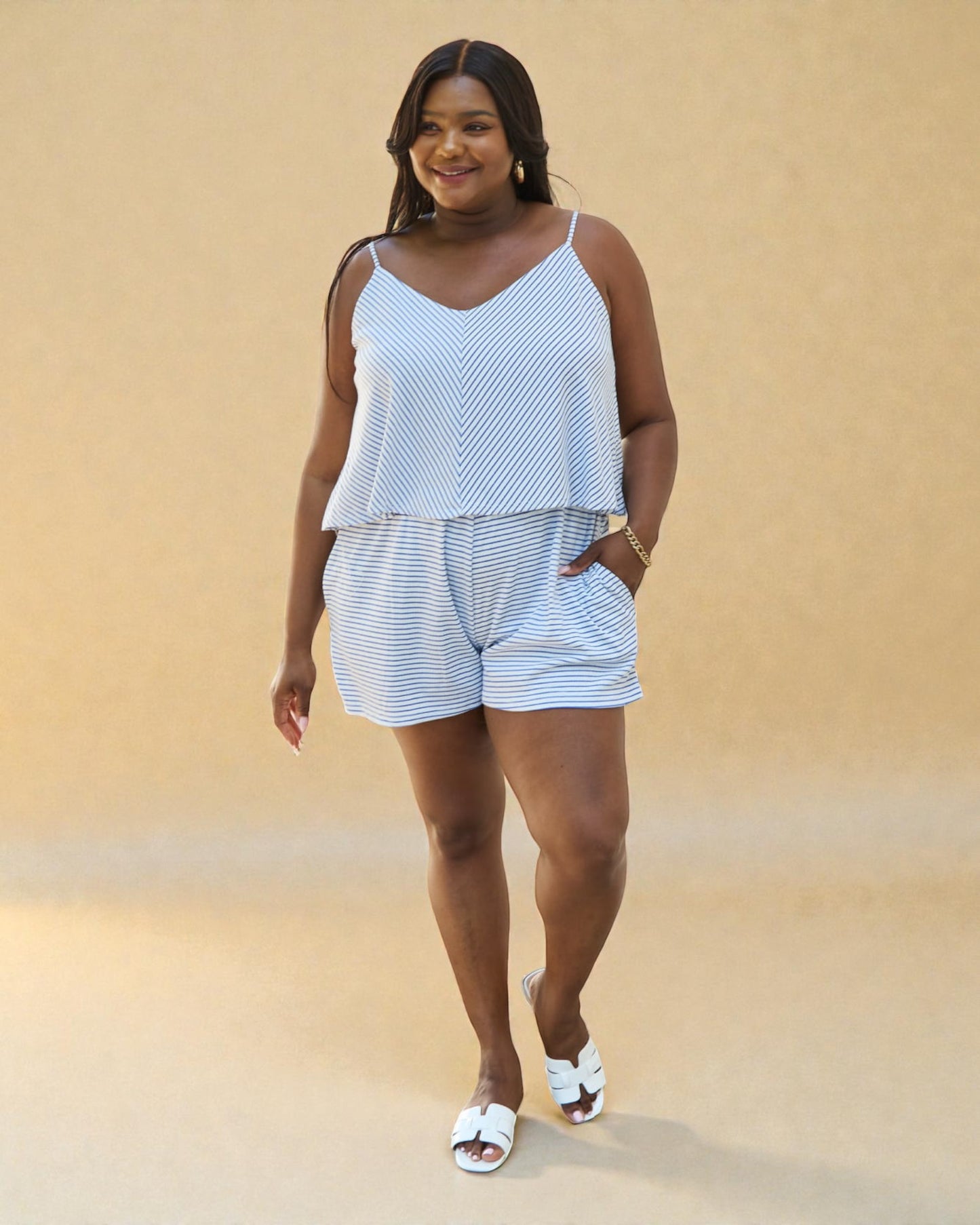 Woman wearing a light blue striped tank top and shorts set against a beige background