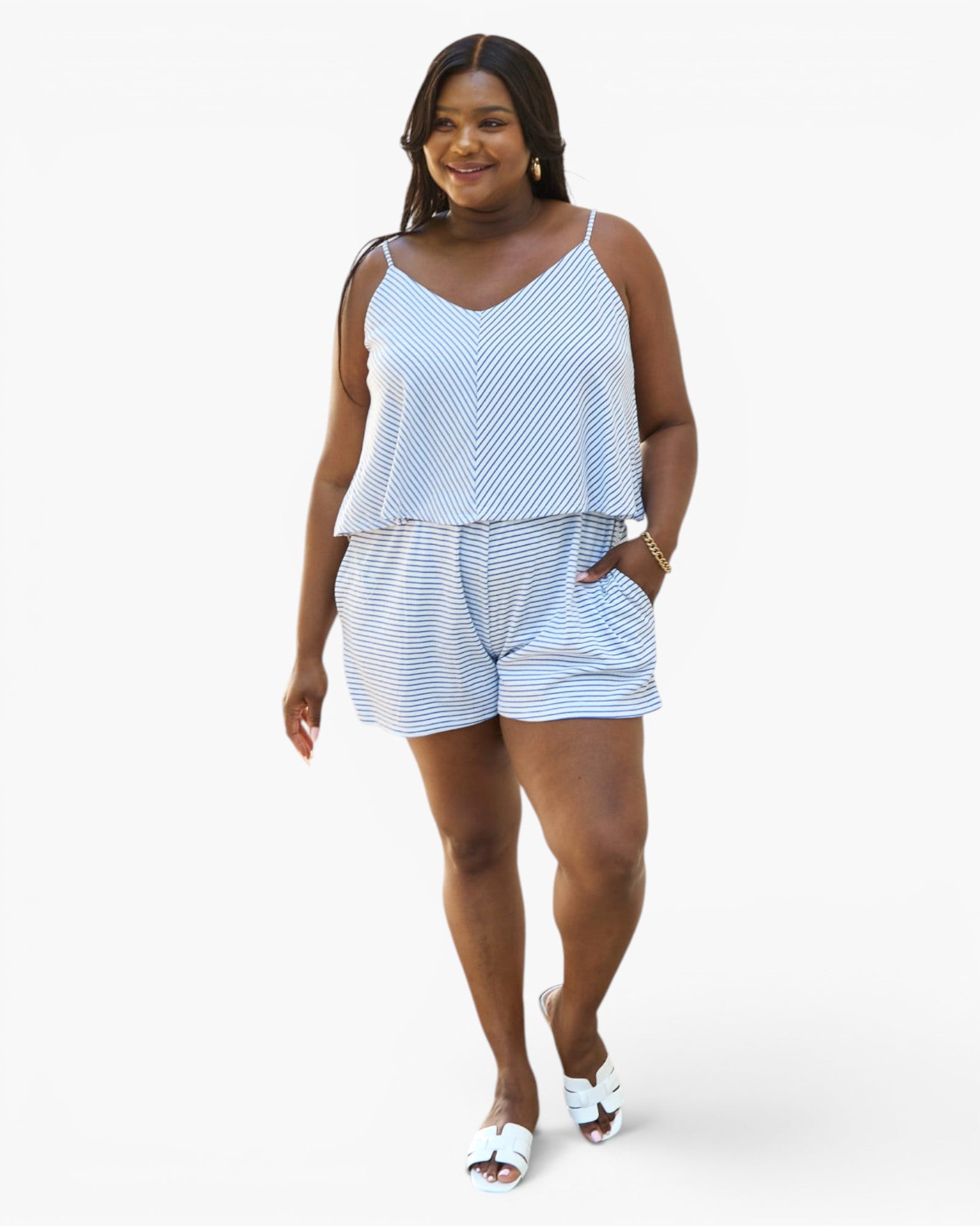 A woman modeling a light blue and white striped two-piece set consisting of a spaghetti-strap camisole top and matching shorts, paired with white slide sandals, against a plain white studio background.