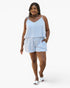 A woman modeling a light blue and white striped two-piece set consisting of a spaghetti-strap camisole top and matching shorts, paired with white slide sandals, against a plain white studio background.