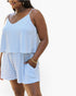 A woman wearing a light blue and white striped camisole top and matching shorts with side pockets, shown against a plain white background.