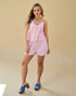 Woman wearing a pink and white checkered outfit with blue sandals on a beige background