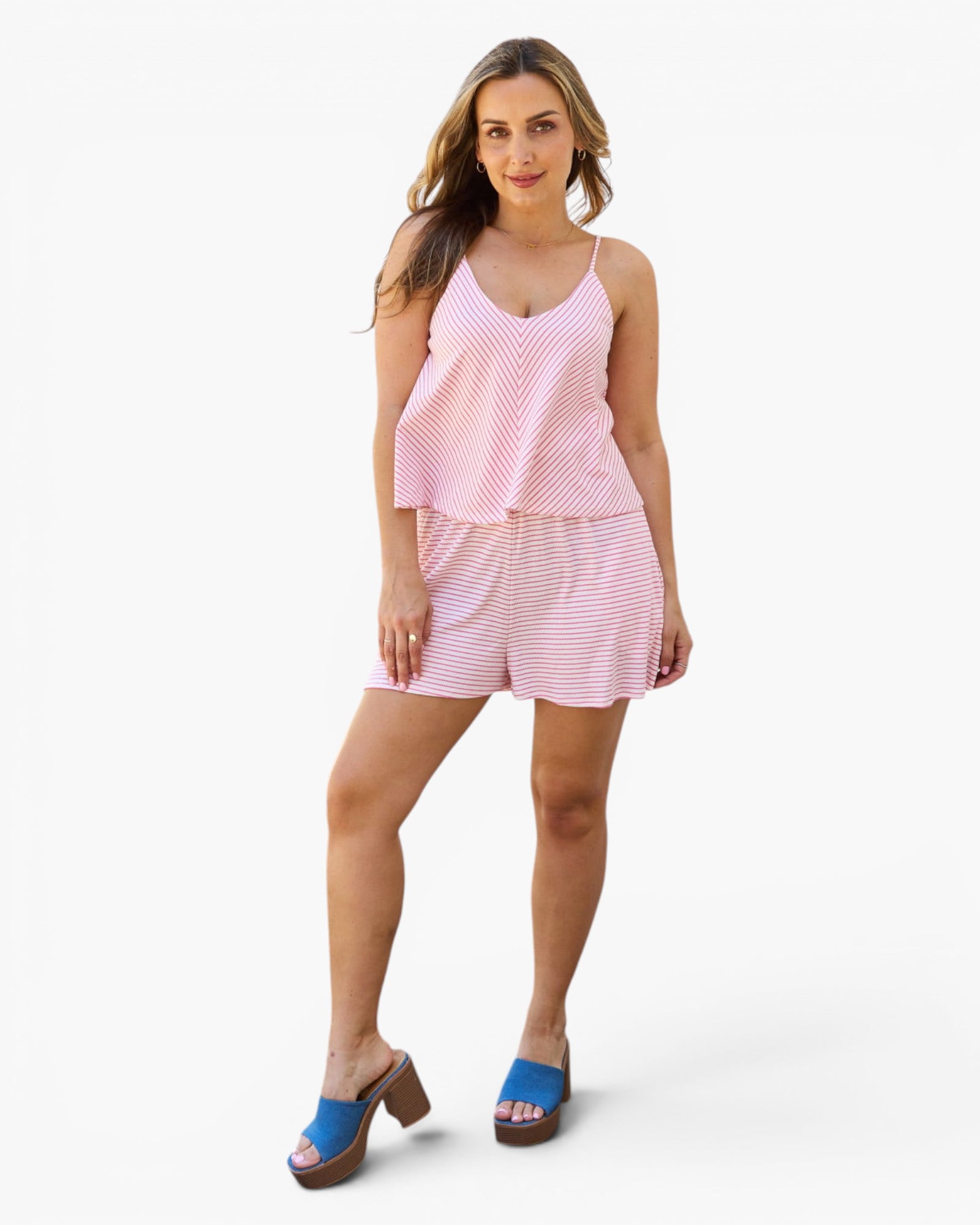 A woman modeling a two-piece matching set consisting of a light pink and white striped camisole top and shorts, paired with blue slide sandals, against a plain white studio background.