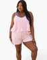 A woman modeling a light pink two-piece set consisting of a sleeveless camisole top with thin straps and matching striped shorts, set against a plain white background.