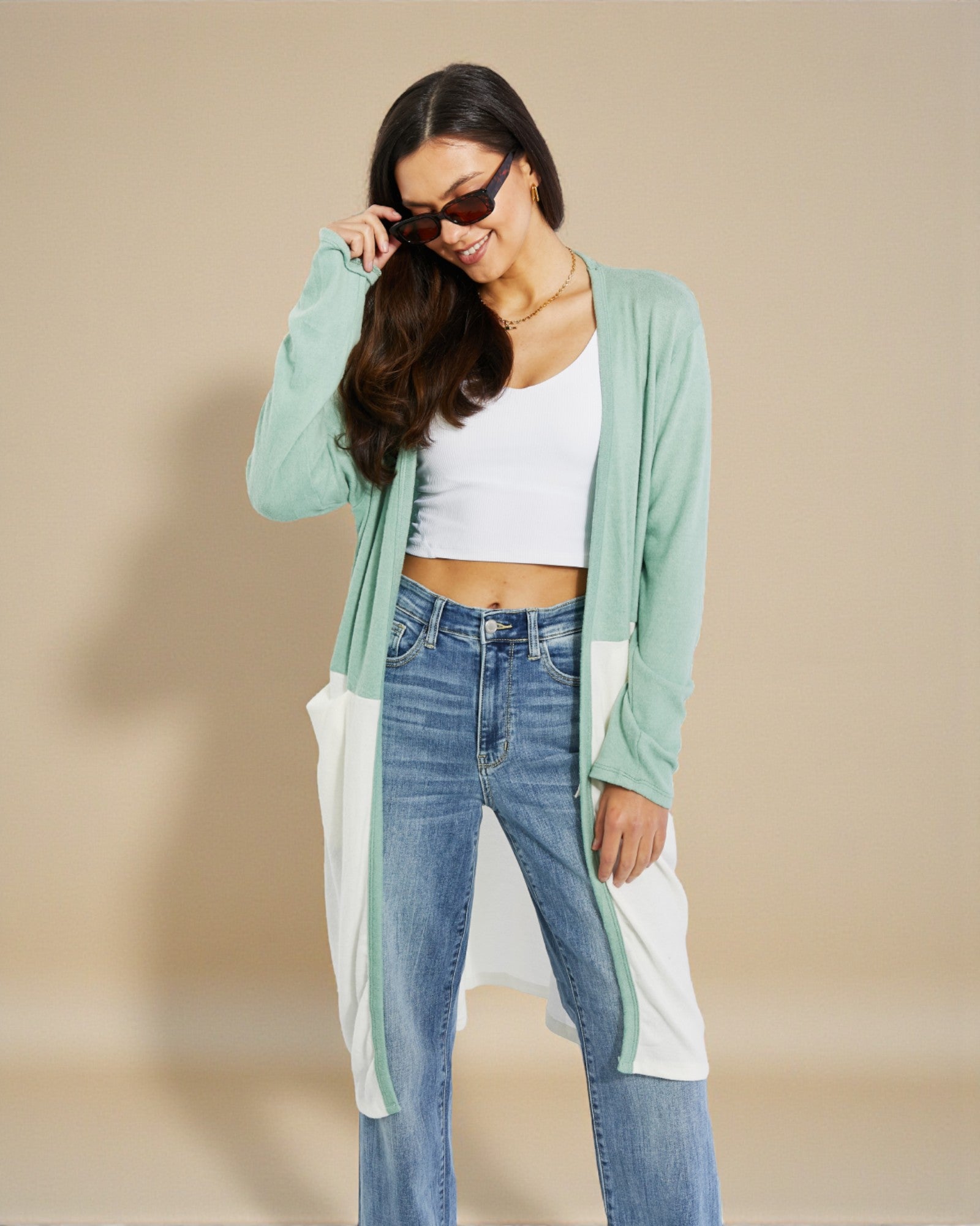 Woman wearing a light green cardigan, white top, and blue jeans on a beige background