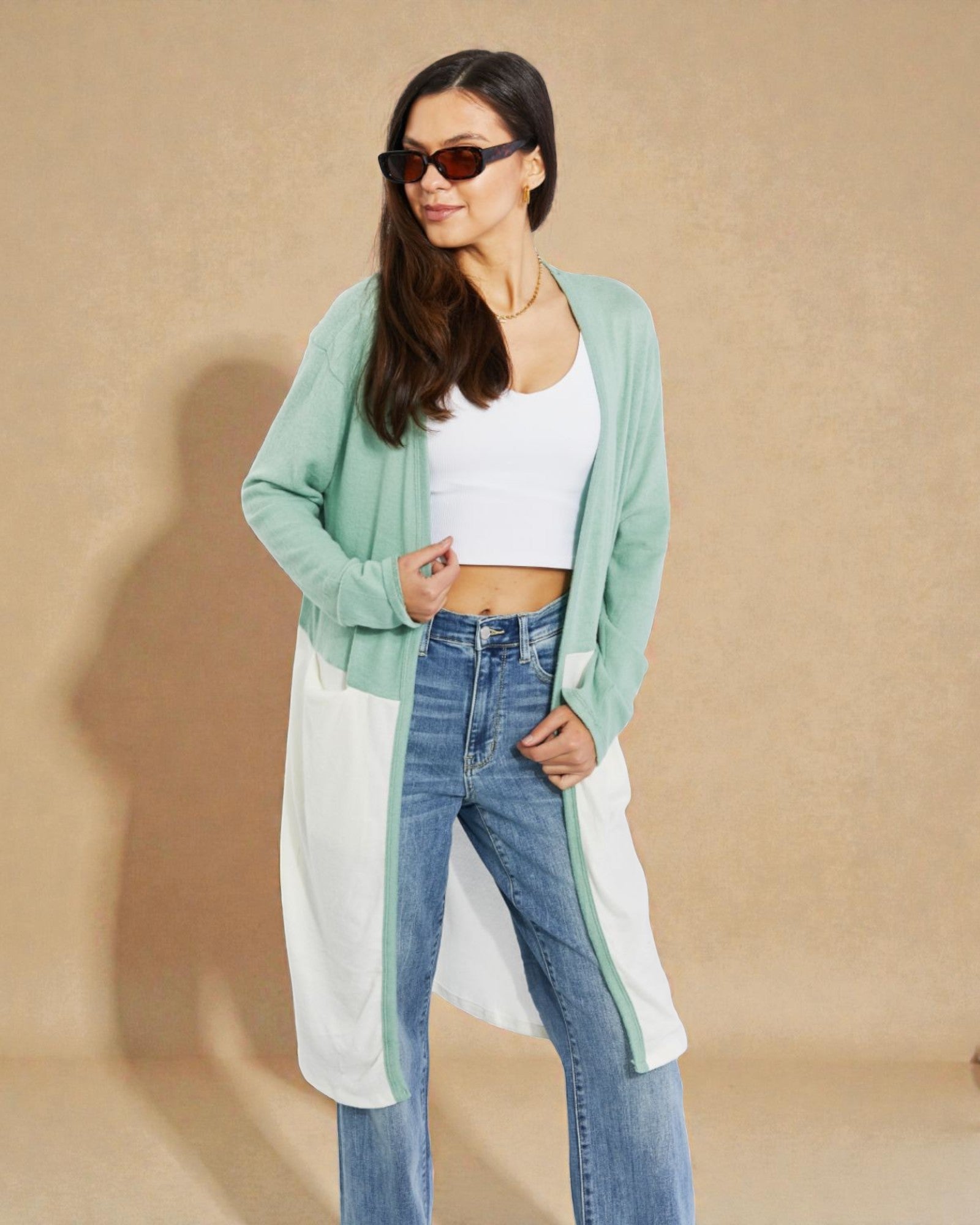 Woman wearing a green cardigan, white top, and blue jeans against a beige background