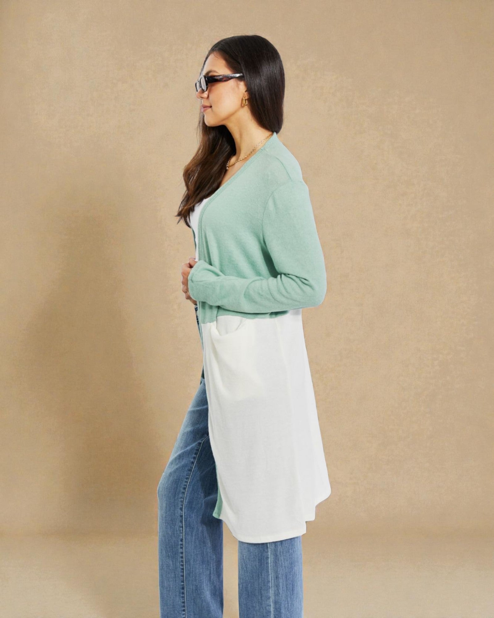 Woman wearing a light green sweater over a white shirt with blue jeans on a beige background