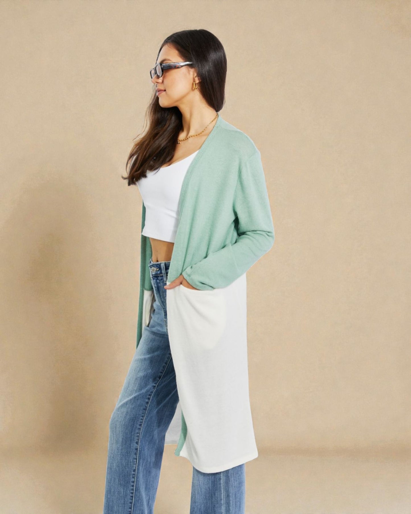 Woman wearing a green cardigan, white top, and blue jeans against a beige background