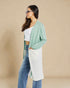 Woman wearing a green cardigan, white top, and blue jeans against a beige background