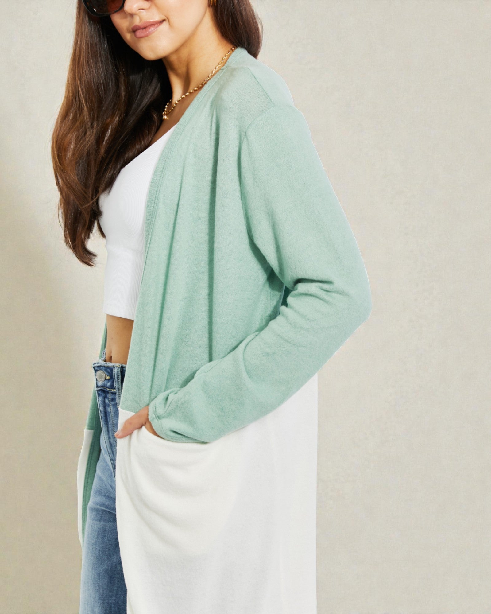 Woman wearing a light green cardigan over a white top and jeans on a beige background