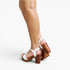 White platform sandals with brown block heels and straps, shown on a model's feet against a light gray studio background.