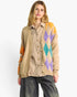 A woman modeling a beige cardigan with a colorful argyle pattern on the front and sleeves, worn over a brown and beige checkered shirt and dark gray jeans, against a plain white background.
