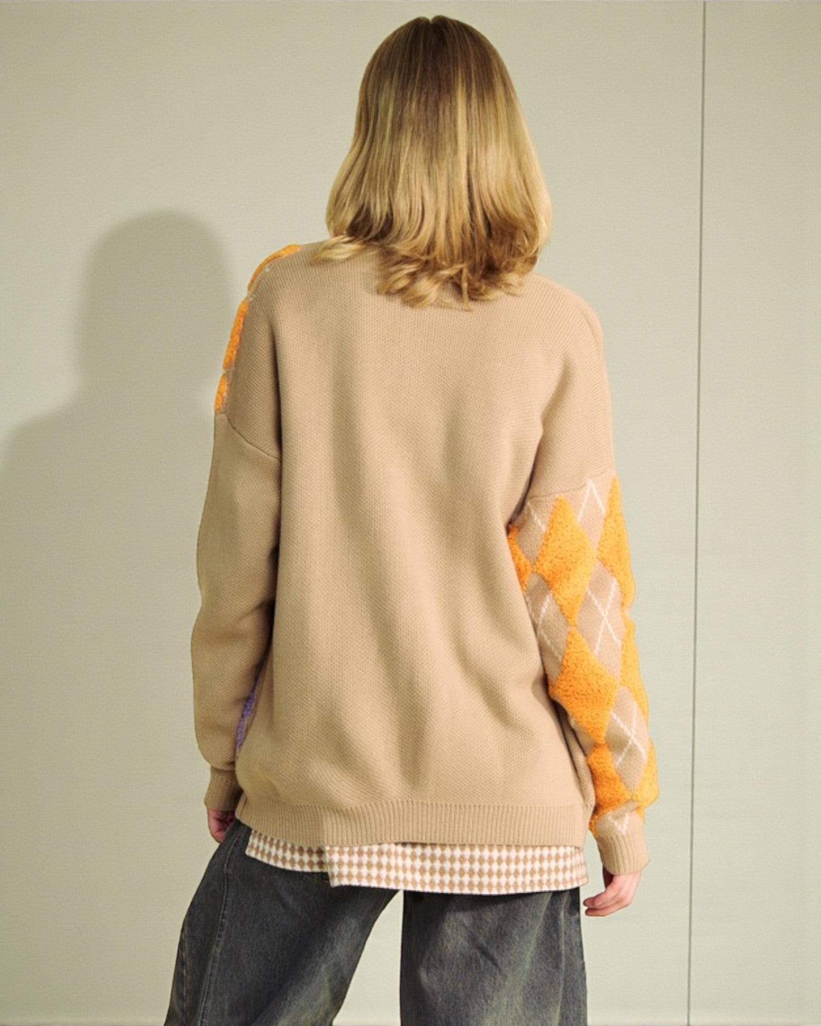 Person wearing a beige sweater with orange sleeves against a plain background