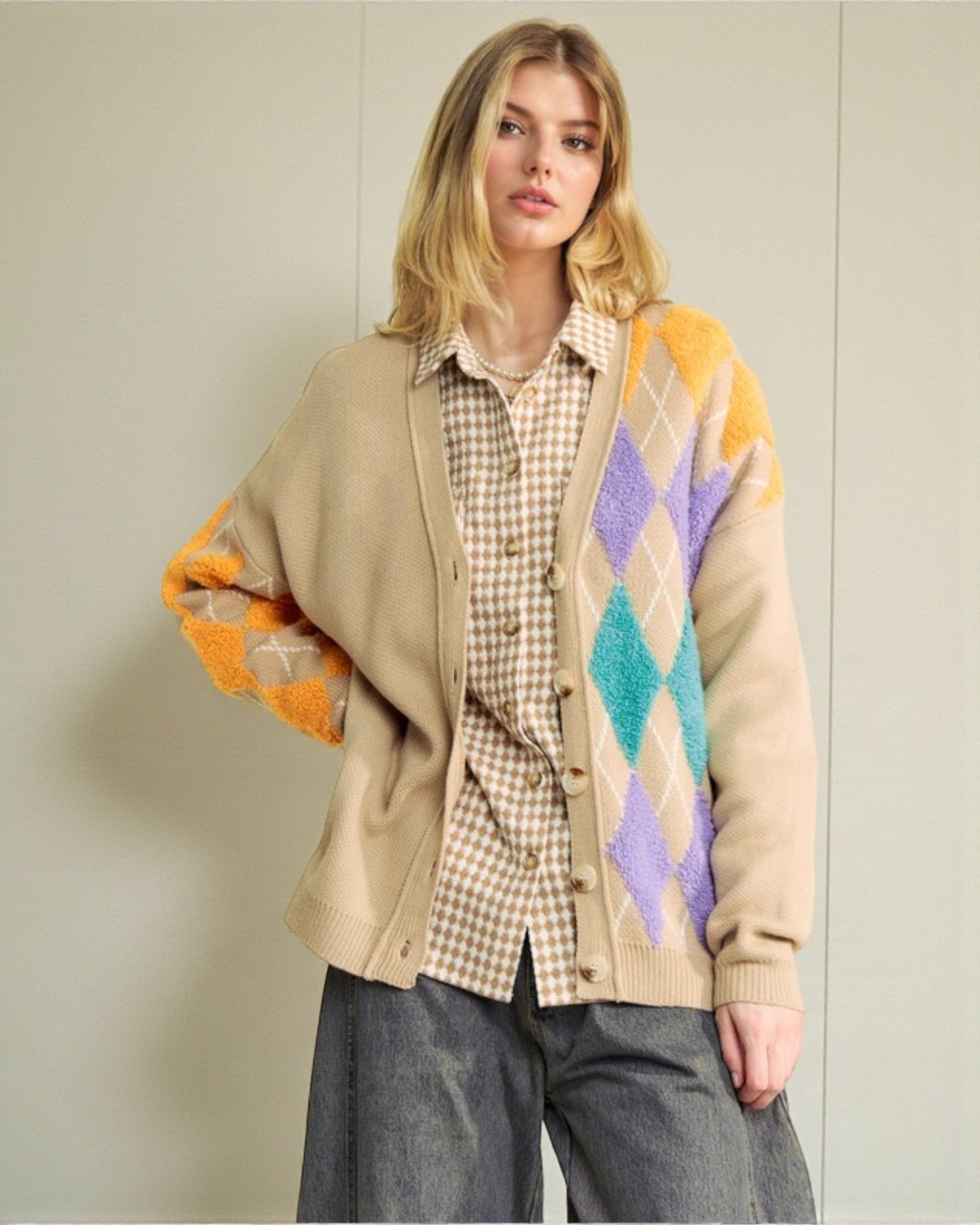 Woman wearing a beige cardigan with colorful diamond pattern over a plaid shirt and gray pants.