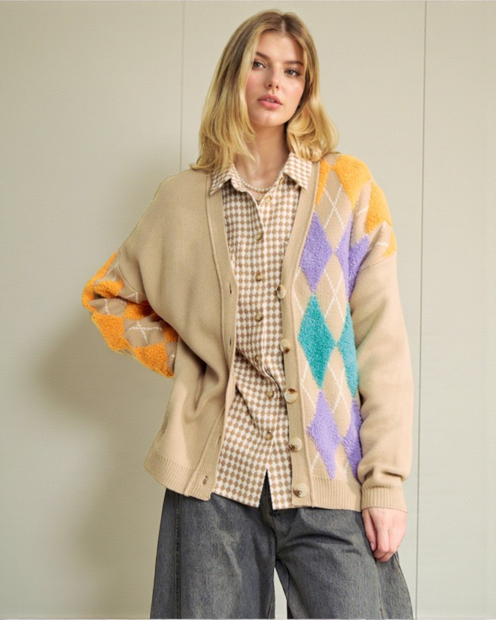 Woman wearing a beige cardigan with colorful diamond pattern over a plaid shirt and gray pants.