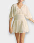 Woman wearing a light-colored romper on a plain background