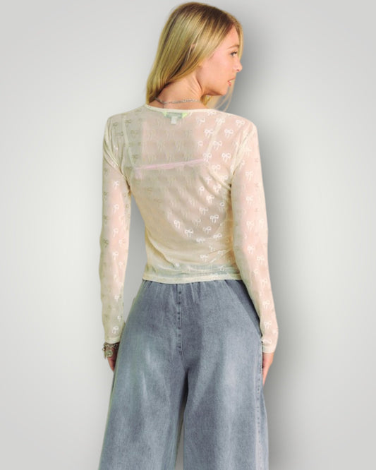 Woman wearing a sheer long-sleeve top and gray pants against a plain background