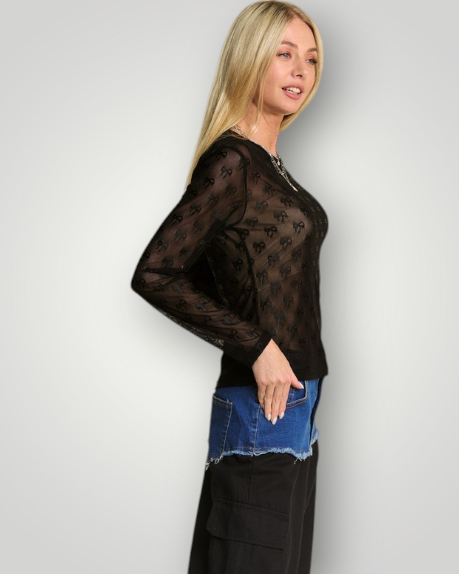 Woman wearing a black sheer top with long sleeves and a blue denim skirt against a white background