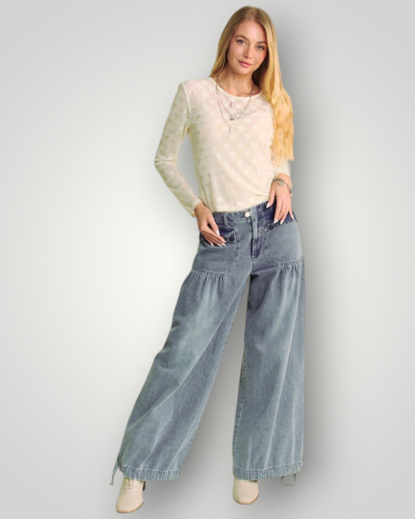 Woman wearing a beige top and blue jeans against a plain background