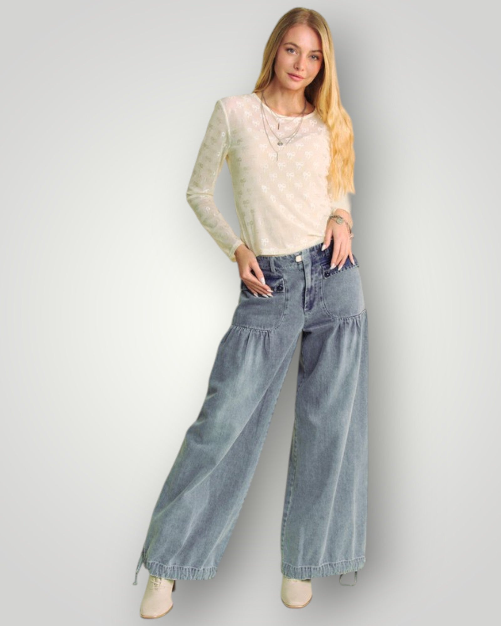 Woman wearing a beige top and blue jeans against a plain background