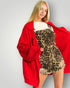 Woman wearing a red coat over a leopard print dress on a plain background