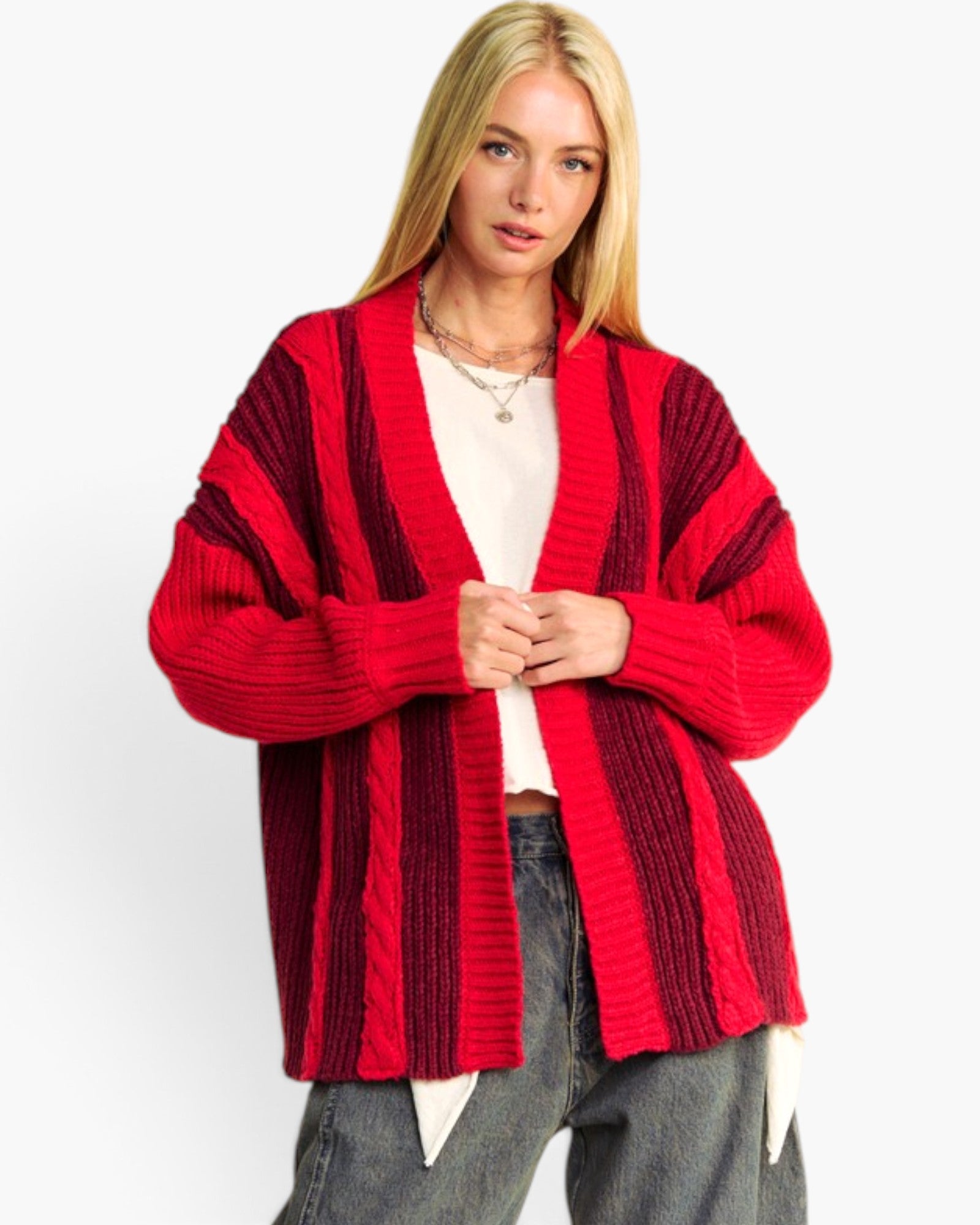 A blonde woman wearing a red and dark red striped open-front knit cardigan over a white top and gray jeans, photographed against a plain light gray studio background.