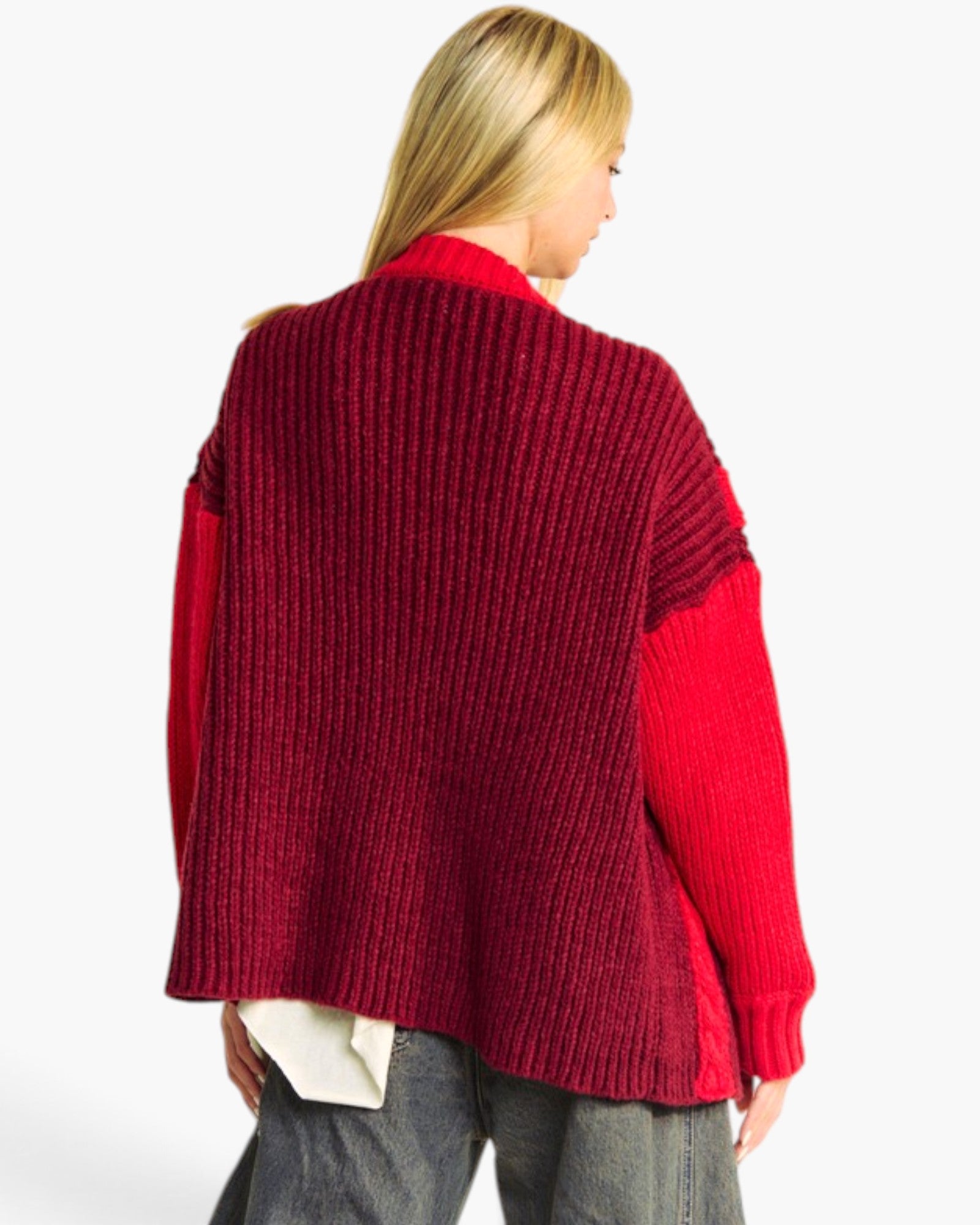 A woman shown from the back wearing a chunky knit cardigan with a deep burgundy back and bright red sleeves, paired with gray jeans against a plain white background.