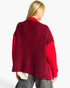 A woman shown from the back wearing a chunky knit cardigan with a deep burgundy back and bright red sleeves, paired with gray jeans against a plain white background.