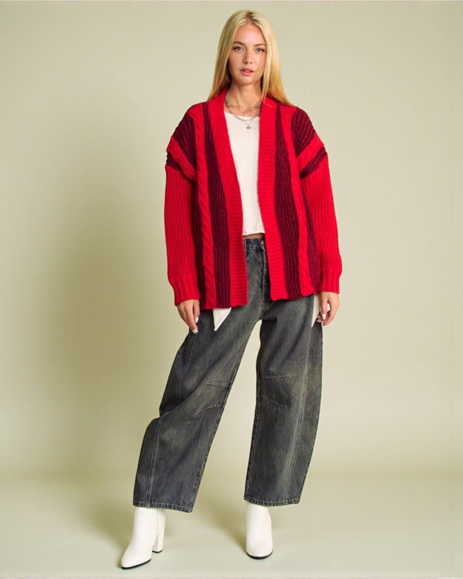 Person wearing a red cardigan, white shirt, and dark jeans on a beige background