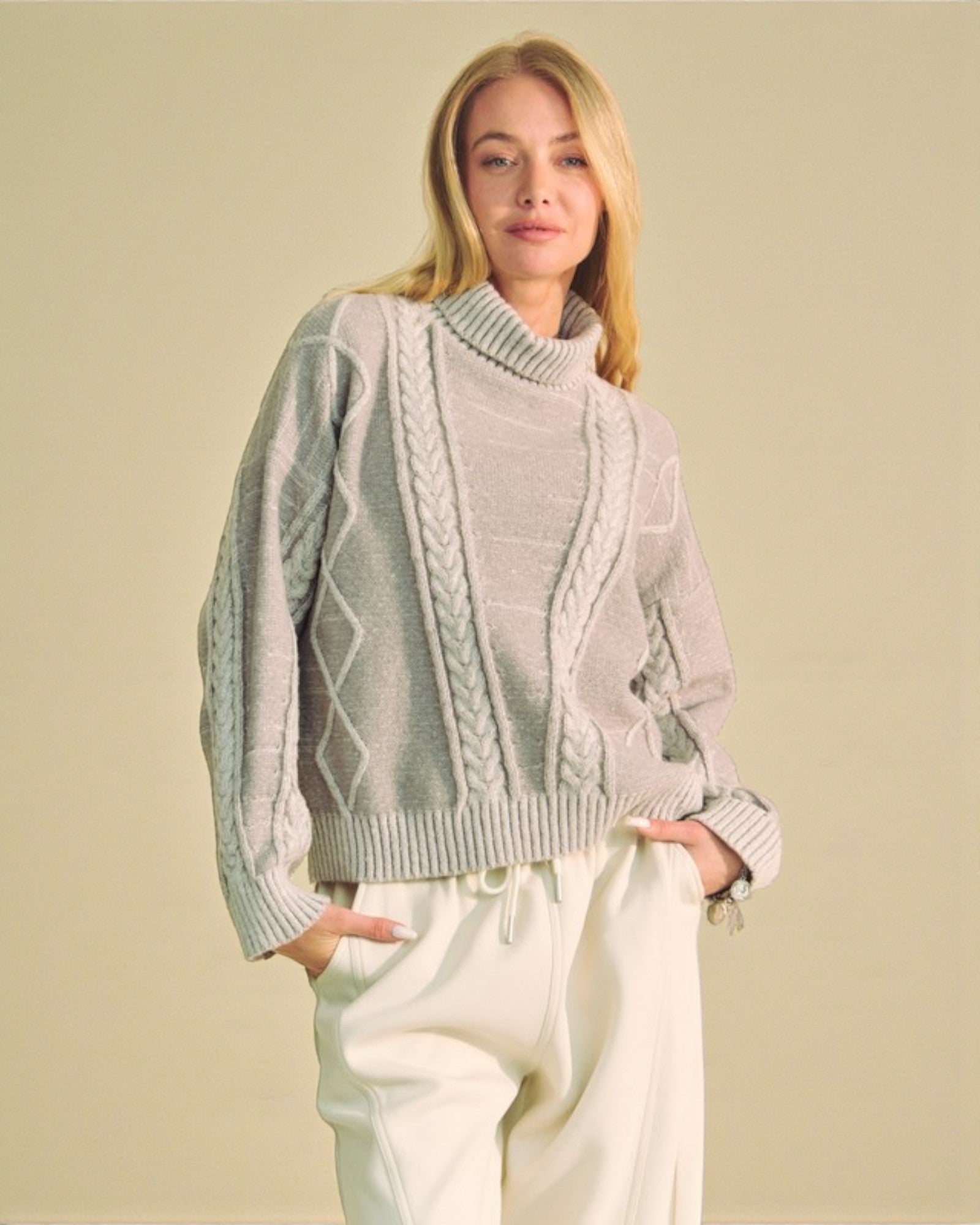 Woman wearing a light gray turtleneck sweater with cable knit details on a beige background