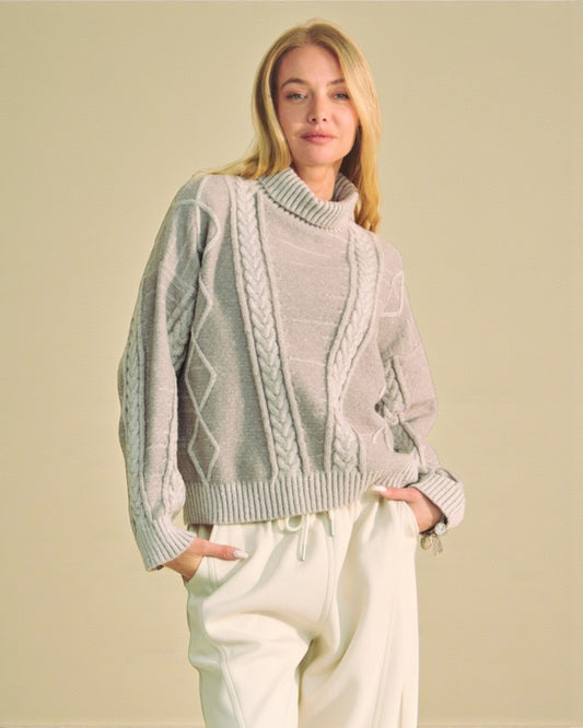 Woman wearing a light gray turtleneck sweater with cable knit details on a beige background