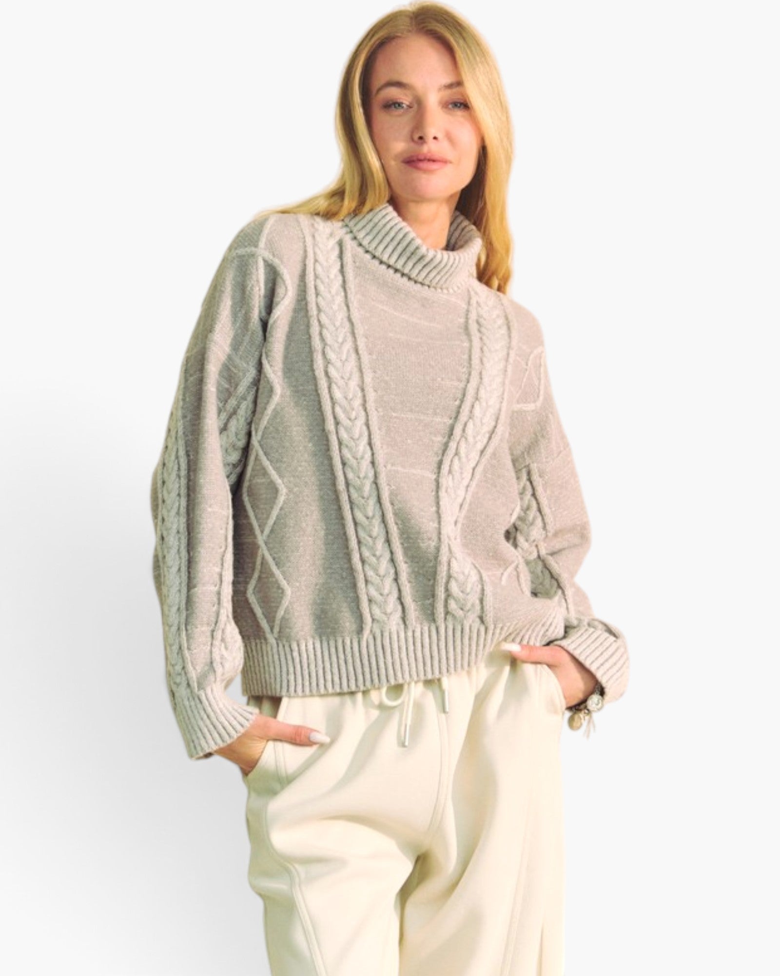 A woman modeling a light beige cable-knit mock-neck sweater with cream sweatpants against a plain white studio background.