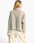 A woman shown from the back wearing a cropped, light taupe knit sweater with textured cable and diamond patterns, paired with cream-colored trousers, against a plain white background.