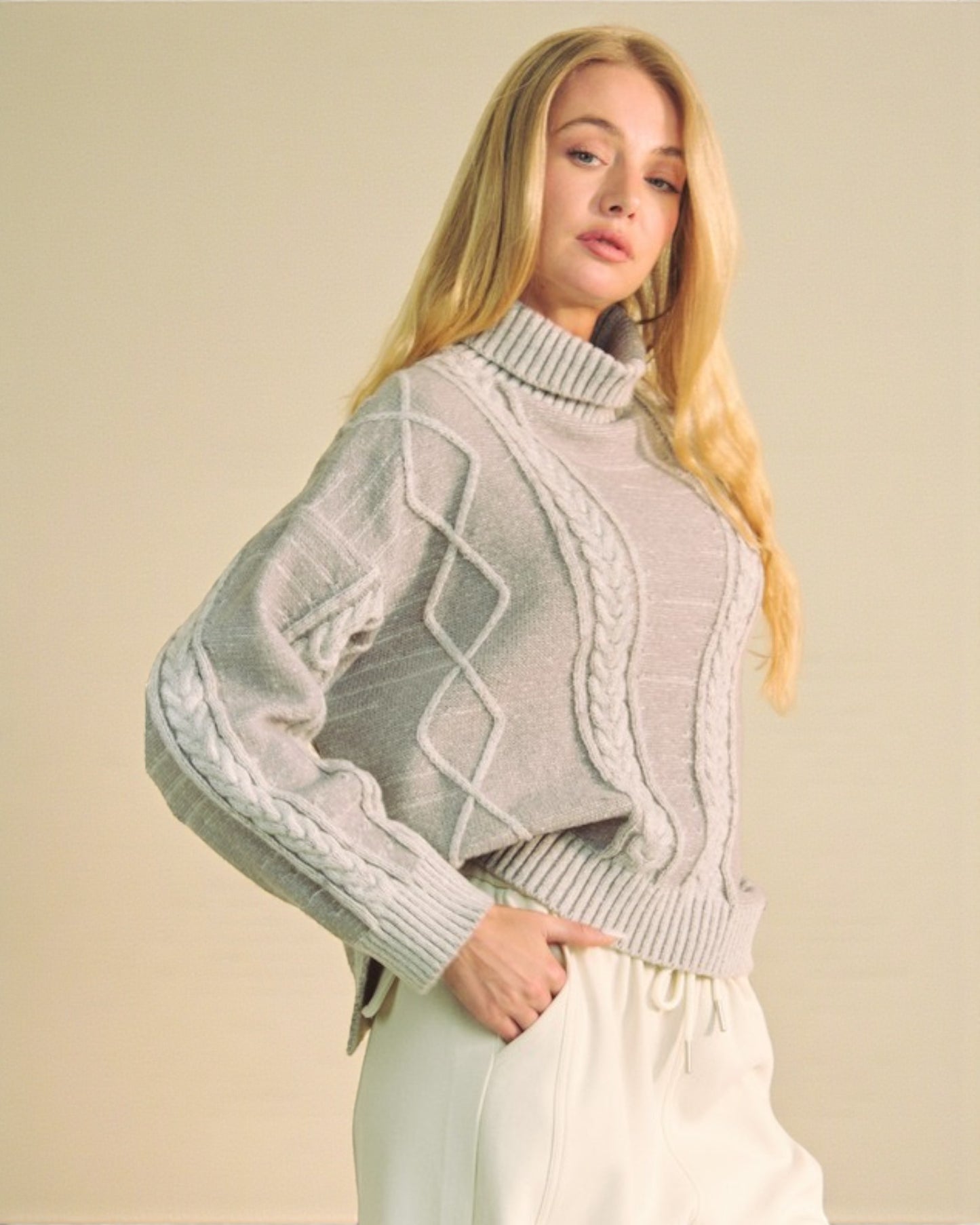 Woman wearing a light gray cable knit sweater against a beige background