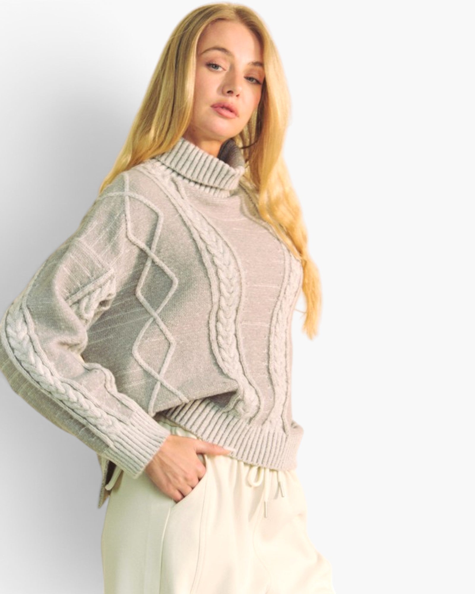 A blonde woman wearing a light beige cable-knit mock-neck sweater and cream drawstring trousers, photographed against a clean white studio background.
