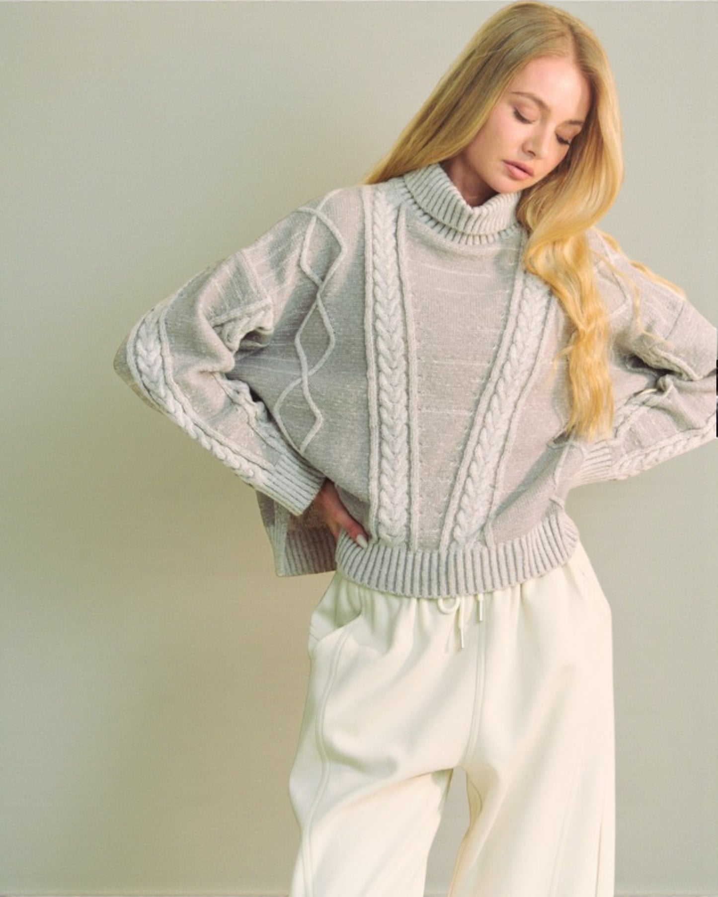 Woman wearing a light gray cable knit sweater with a plain background