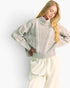 A woman wearing a light sage green cable-knit mock-neck sweater and cream-colored sweatpants, posing against a plain white studio background.