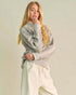 Woman wearing a light gray sweater and white pants against a plain background