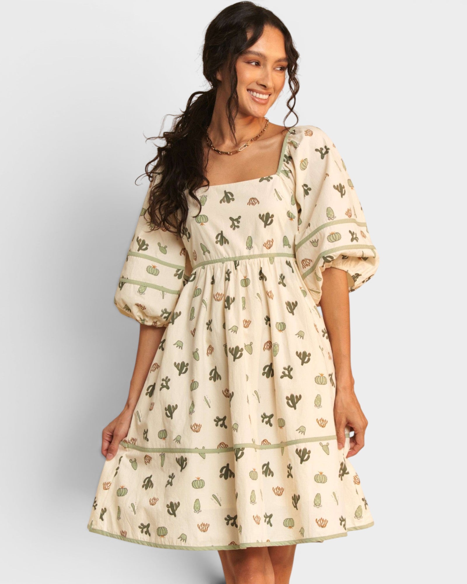 Woman wearing a cream-colored dress with cactus pattern on a plain background