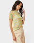 Woman wearing a patterned green and orange shirt with beige pants on a white background