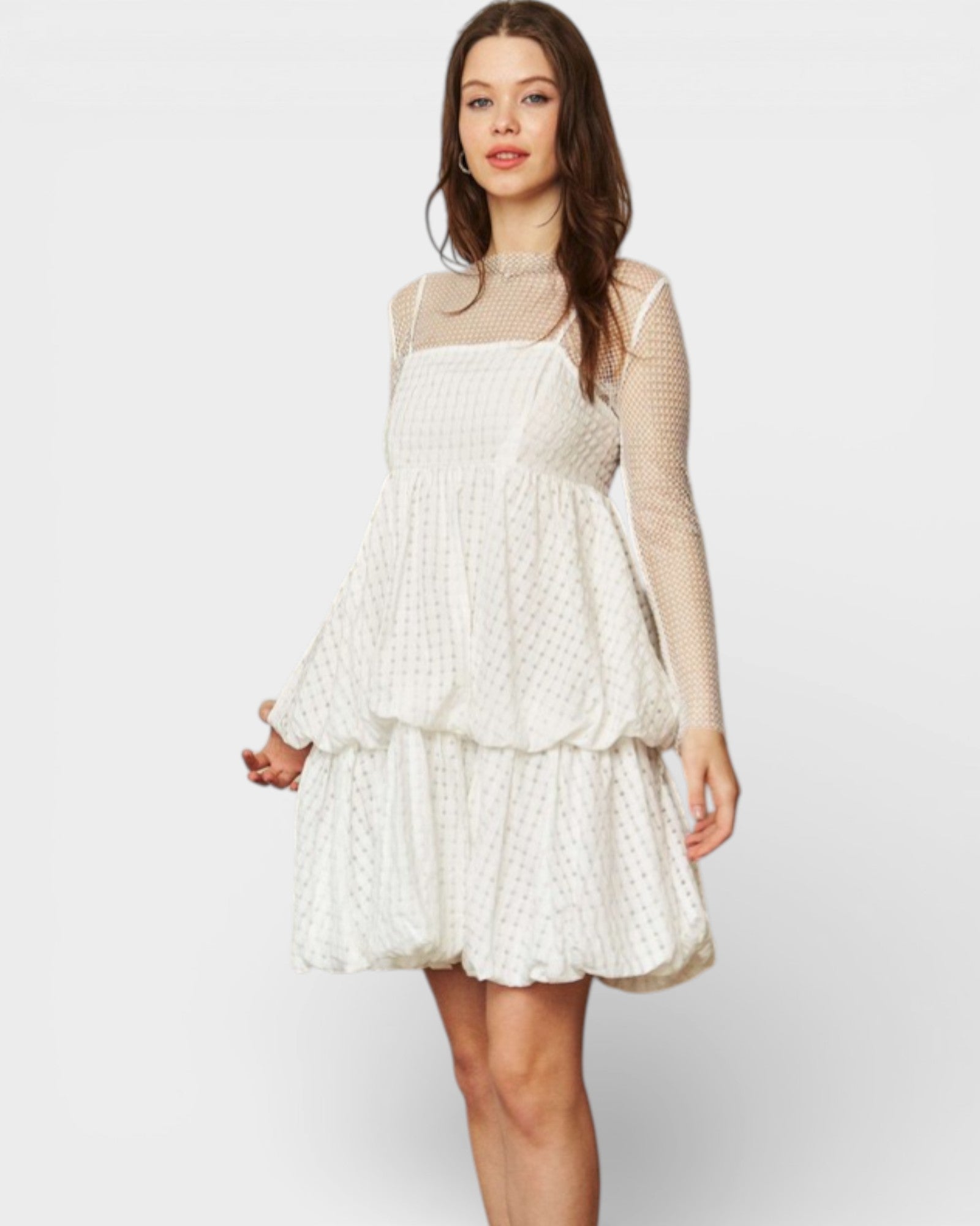 Woman wearing a white lace dress with sheer sleeves on a plain background