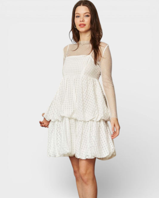 Woman wearing a white lace dress with sheer sleeves on a plain background