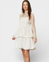 Woman wearing a white lace dress with sheer sleeves on a plain background