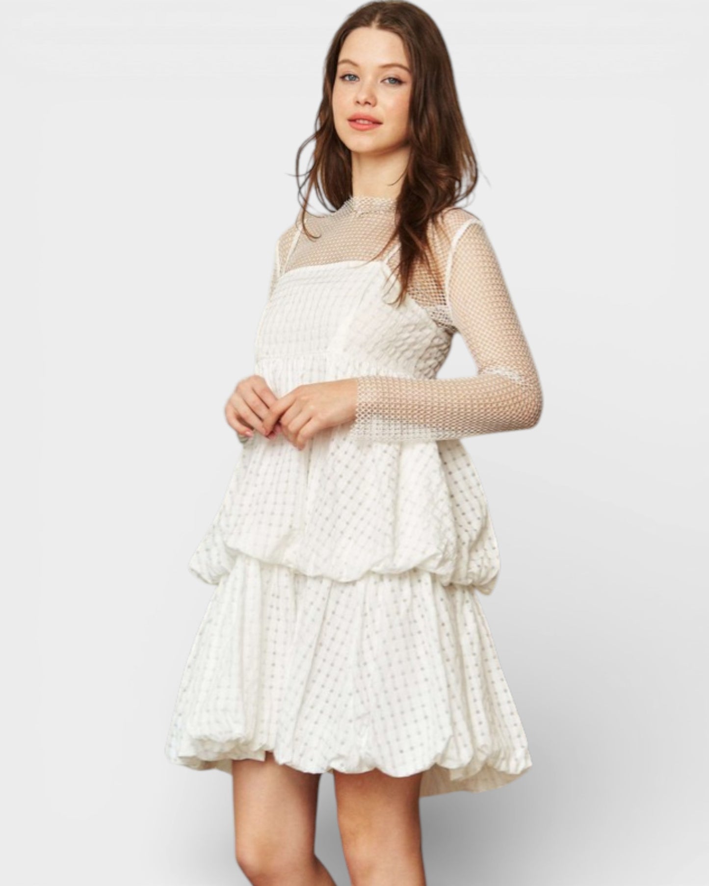 Woman wearing a white dress with sheer sleeves on a plain background